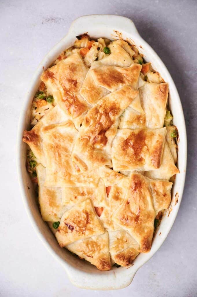 A white oval baking dish filled with a golden-brown chicken pot pie casserole, topped with a lattice of crispy pastry.