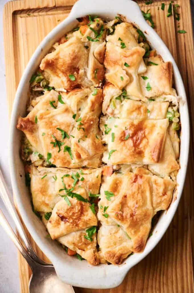 A golden-brown chicken pot pie casserole in a white baking dish, sprinkled with chopped herbs on top.