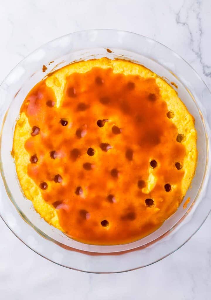 A freshly baked, golden-brown chicken tamale pie in a clear glass dish, with caramel sauce on top and scattered bubbles on the surface.