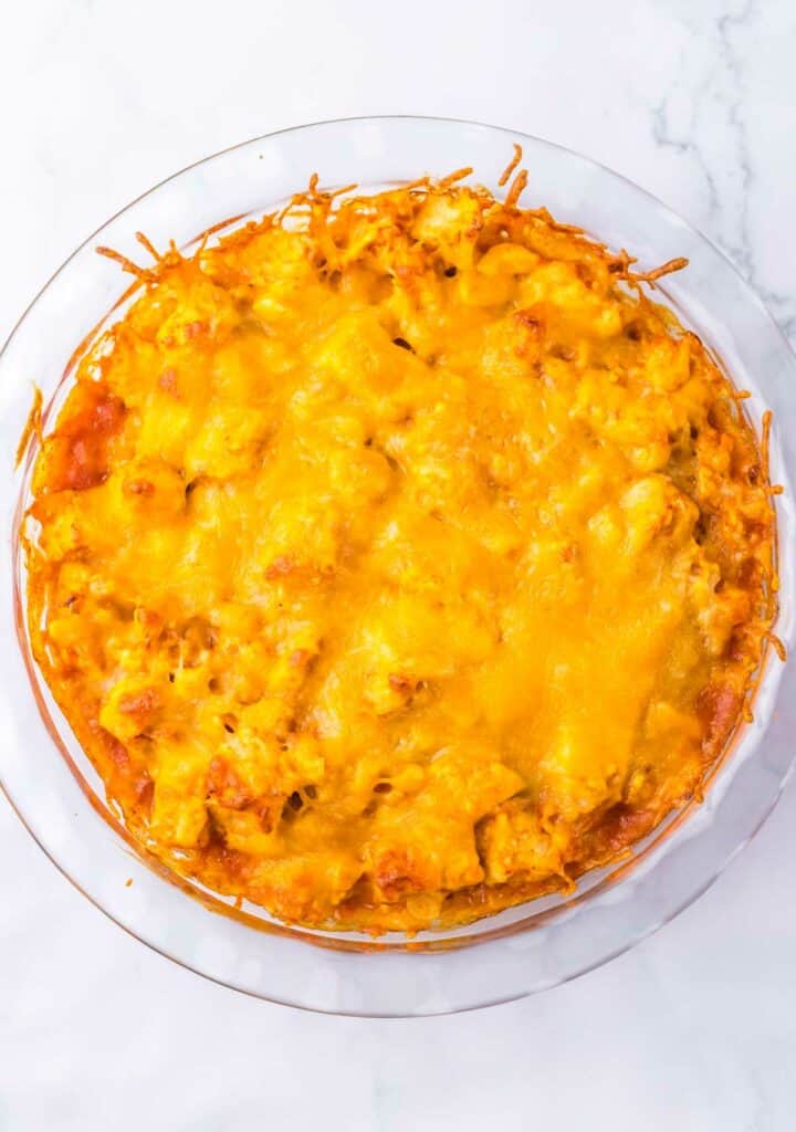 A freshly baked chicken tamale pie in a round glass dish, displayed on a white marble surface.
