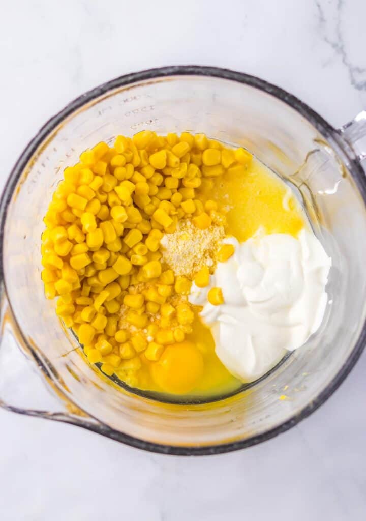 Ingredients for chicken tamale pie including corn, eggs, mayonnaise, and garlic powder in a glass measuring jug, ready for mixing.