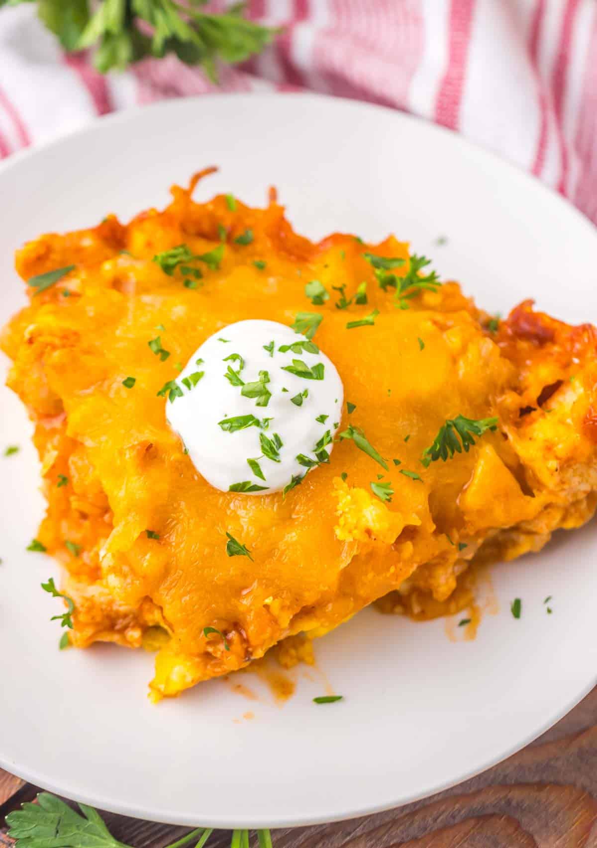 A plate of chicken tamale pie topped with sour cream and garnished with fresh parsley, served on a rustic wooden table.