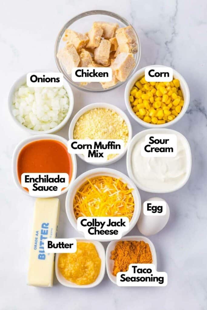Ingredients for a chicken tamale pie recipe laid out on a counter, including onions, chicken, corn, cheese, butter, egg, sour cream, enchilada sauce, corn muffin mix,