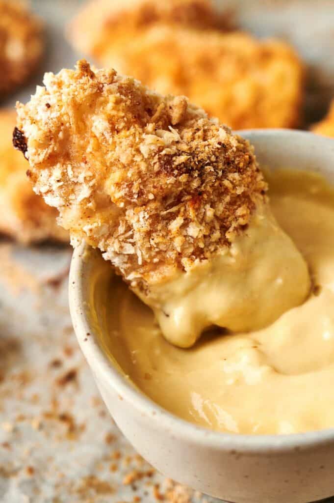 A crispy breaded chicken tender being dipped into a creamy sauce.