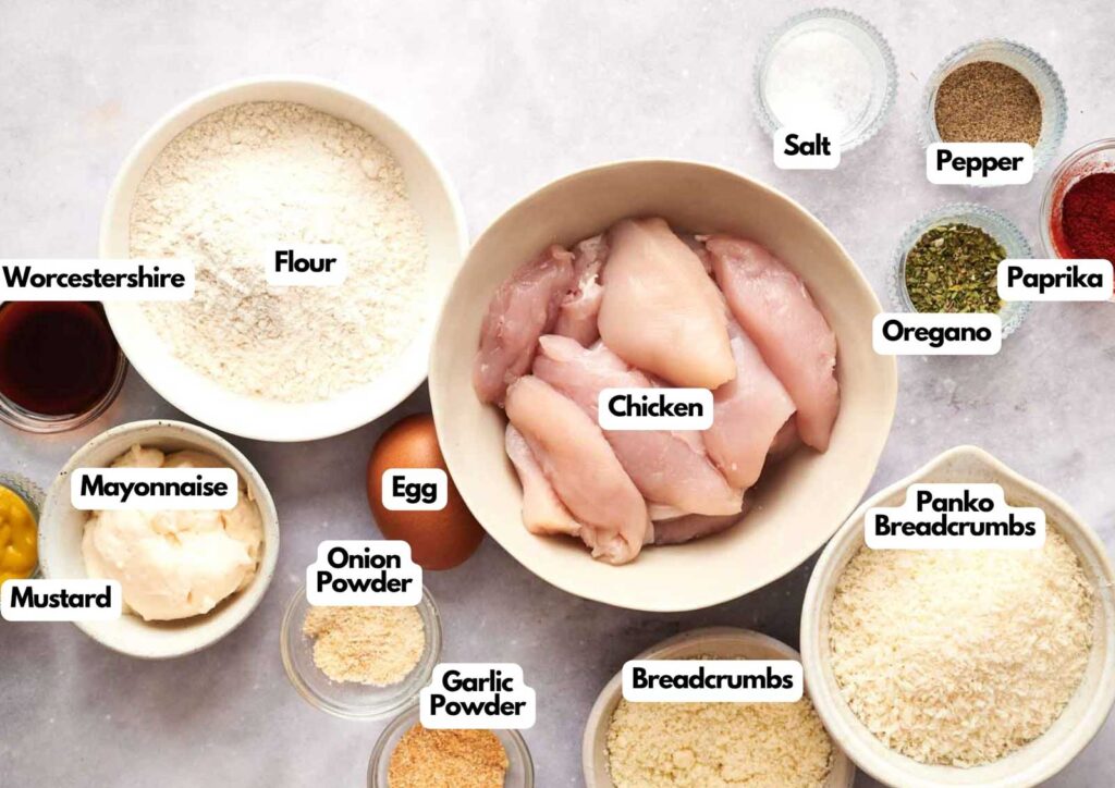 Top-down view of labeled ingredients for chicken tenders, featuring chicken breasts, flour, egg, mayonnaise, mustard, spices, panko breadcrumbs, and seasonings in bowls.