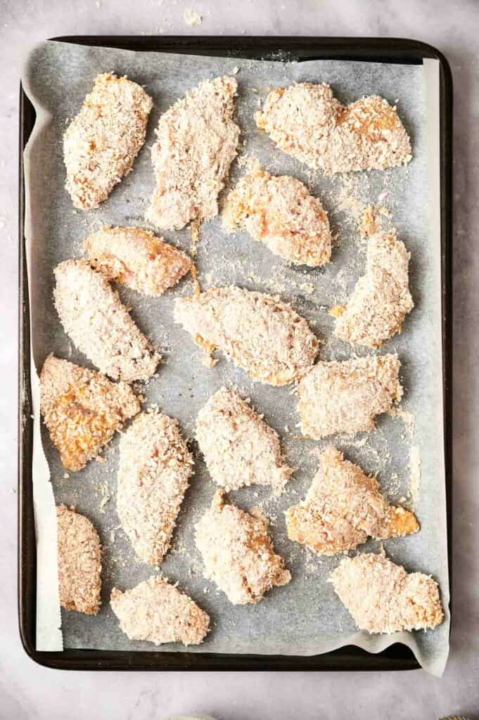 Breaded chicken tenders on a parchment-lined baking sheet.