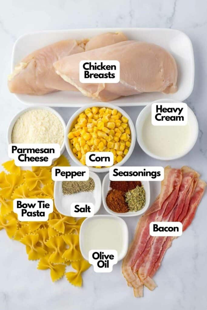Ingredients for a Chicken and Corn Pasta recipe displayed on a countertop, including chicken breasts, heavy cream, parmesan cheese, corn, pasta, bacon, seasoning, and olive oil, labeled individually
