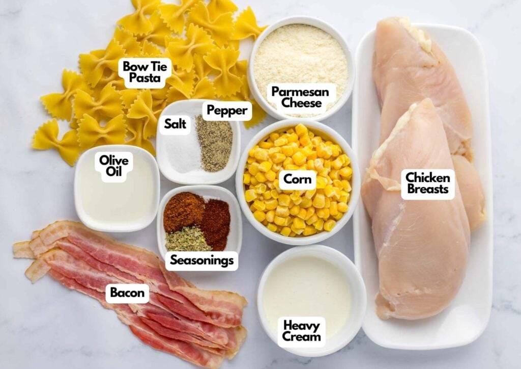 Ingredients for Chicken and Corn Pasta laid out: bow tie pasta, chicken breasts, bacon, corn, heavy cream, parmesan cheese, olive oil, salt, pepper, and seasonings.