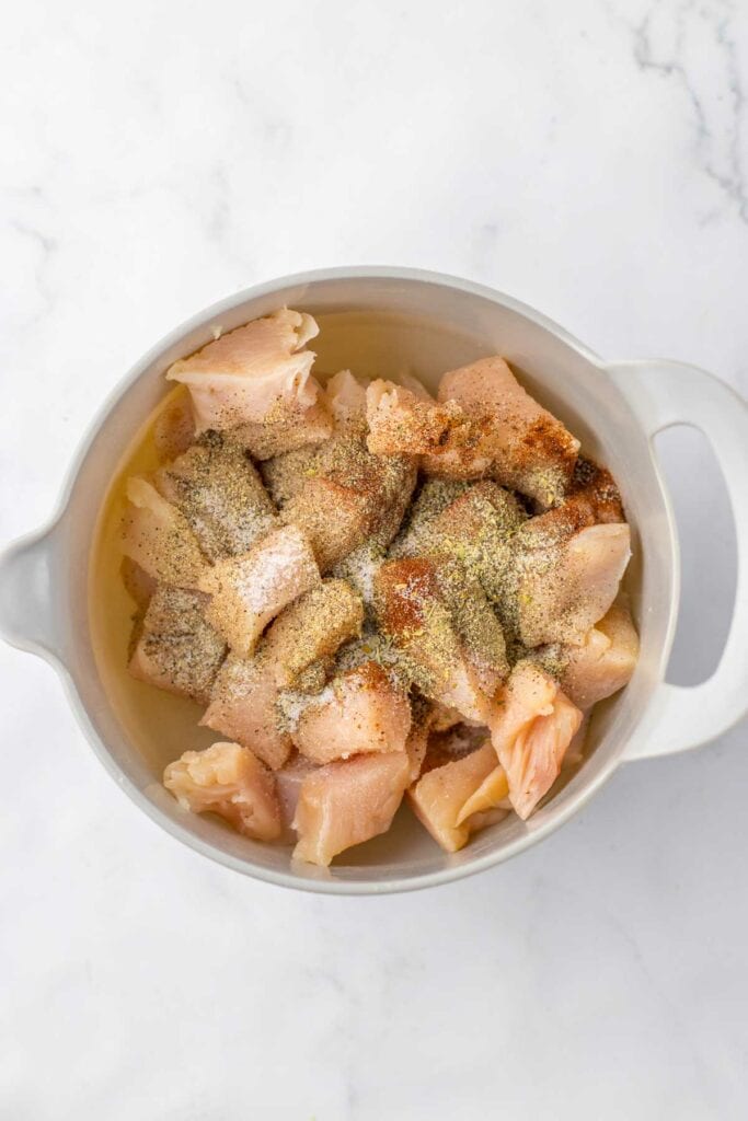 Raw chicken in a pot seasoned with spices, ready for cooking.