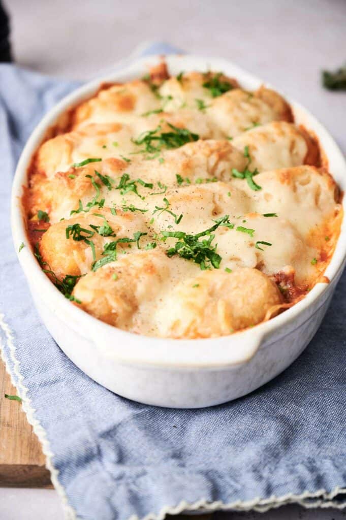 A freshly baked cowboy casserole topped with golden brown biscuits and garnished with chopped parsley, served in a white oval dish.