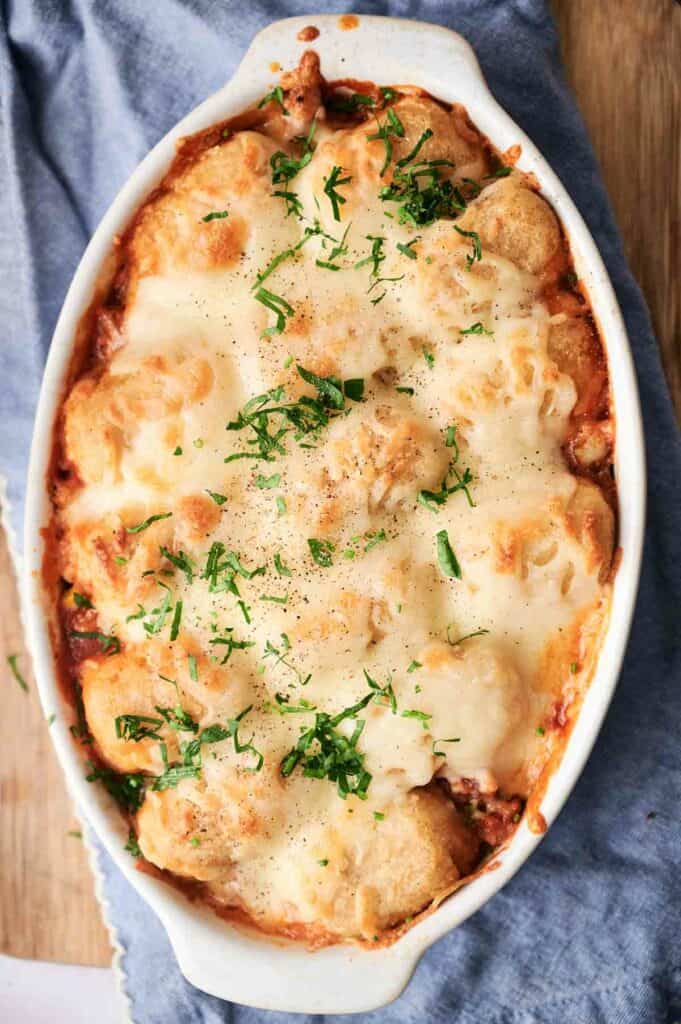 Baked cowboy casserole in a white dish, topped with melted cheese and garnished with chopped herbs.