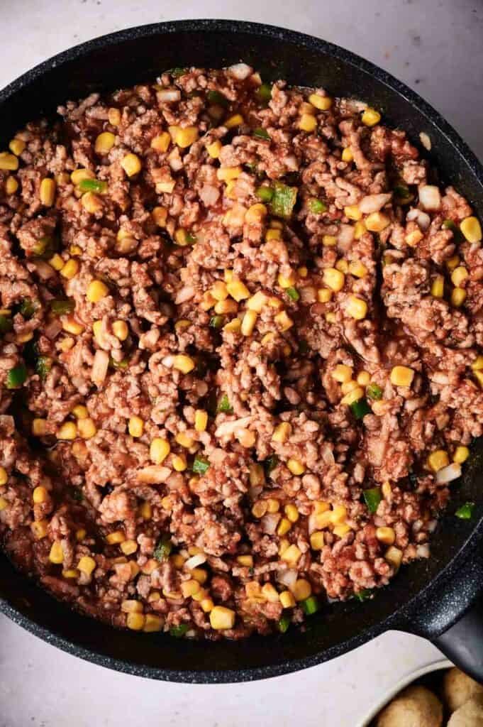 Close-up of a skillet filled with cowboy casserole, including cooked ground beef, corn, and diced green peppers.