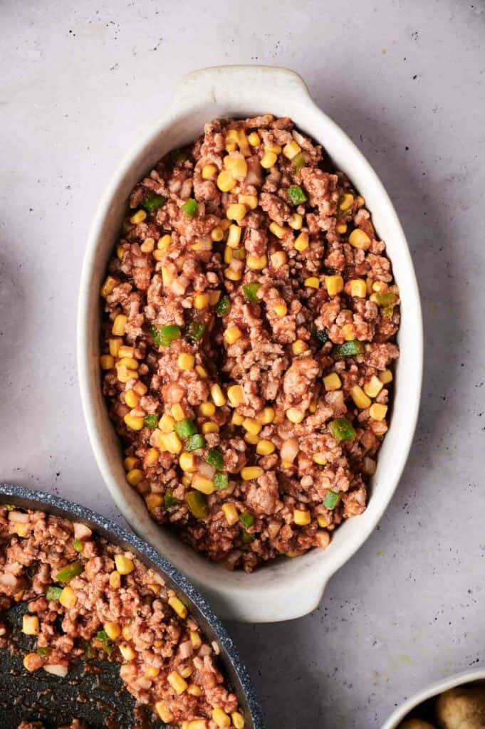 Baked cowboy casserole containing ground meat, corn, and green onions in a white oval dish, viewed from above.