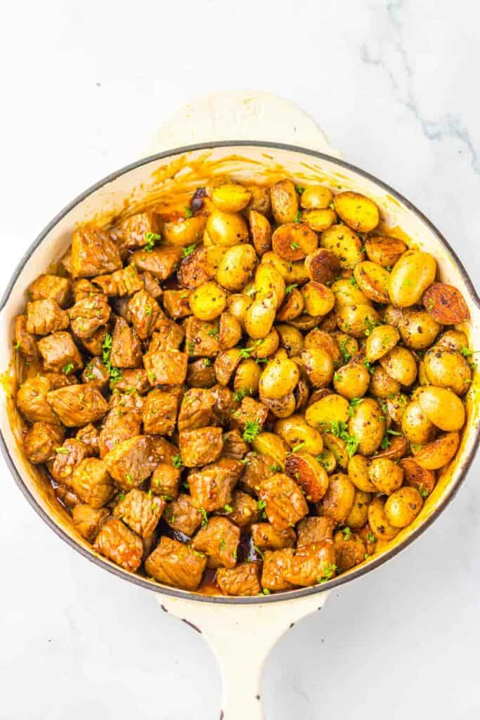 A skillet filled with honey chipotle steak and roasted baby potatoes garnished with parsley.