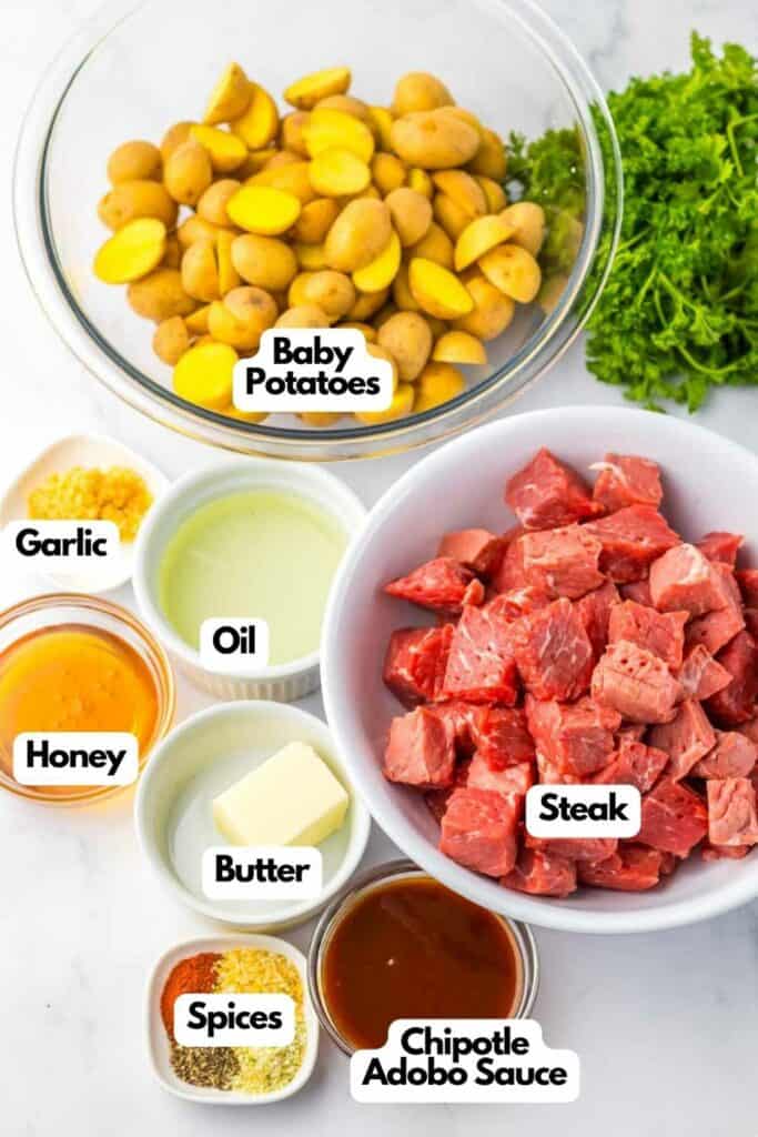 Various ingredients arranged for cooking, including baby potatoes, steak cubes, garlic, honey chipotle sauce, butter, spices, and oil, each in separate bowls.