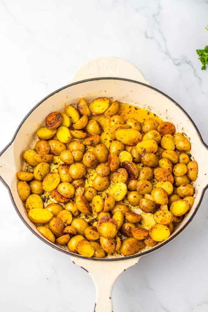 Roasted honey chipotle steak and baby potatoes in a white cast iron skillet on a marble countertop.