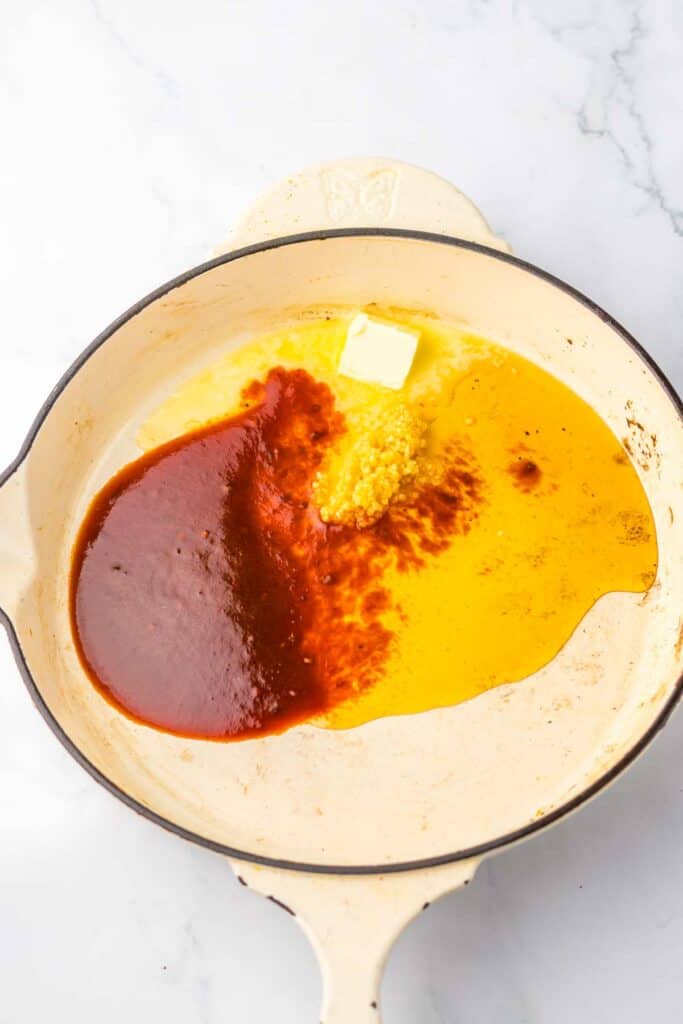 A skillet containing melted butter, tomato sauce, minced garlic, and honey chipotle steak, ingredients prepared for cooking.