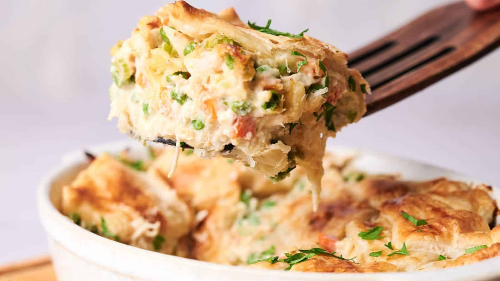 A serving of creamy chicken pot pie casserole with vegetables, lifted on a fork, with a flaky crust and garnished with herbs.