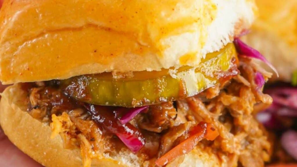 Close-up of pulled pork sliders with pickles and red cabbage on a bun.