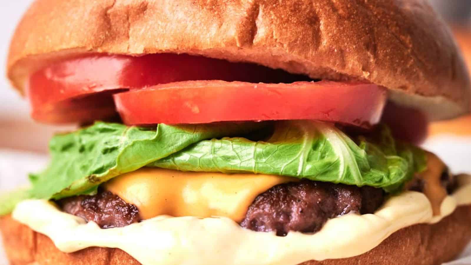 Close-up of a copycat smash burger with lettuce, tomato, and a thick beef patty on a sesame seed bun.