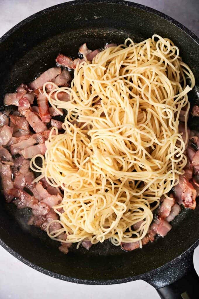 Cooked pasta and bacon in a skillet.
