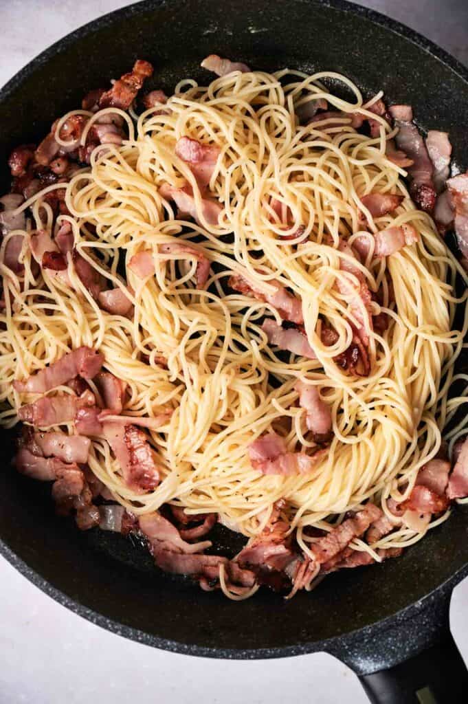 Combined Cooked pasta and bacon in a skillet.