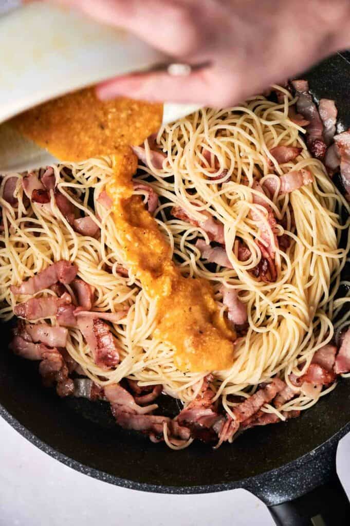 Egg mixture poured into a skillet with pasta and bacon.