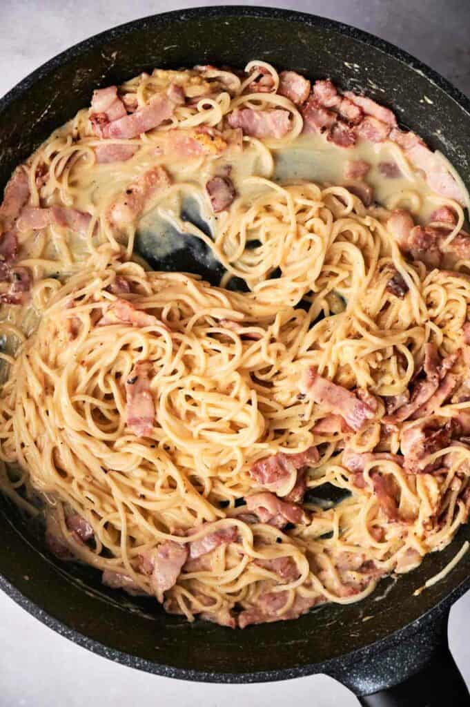 combined egg mixture and pasta in a skillet with pasta and bacon.