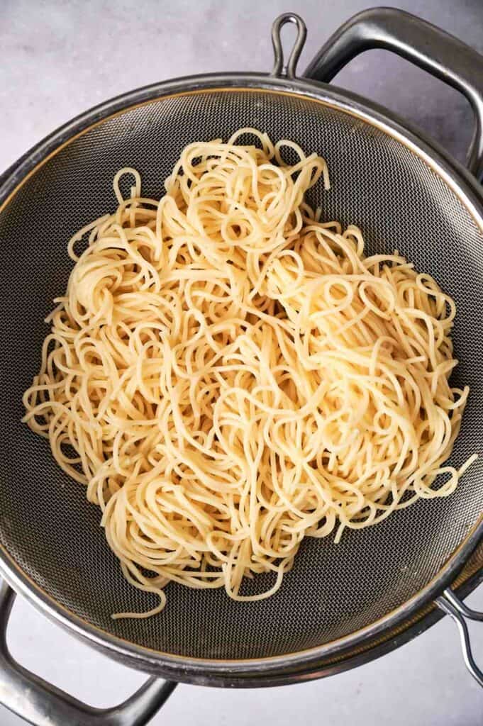 Spaghetti drained in a metal strainer.