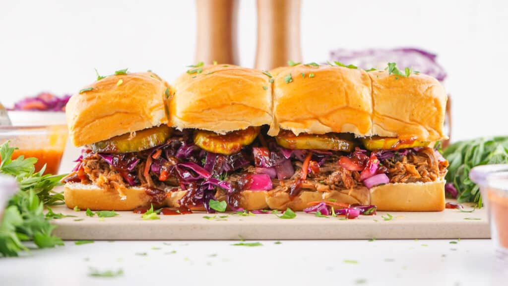 A row of pulled pork sliders with purple slaw and pickles on brioche buns.