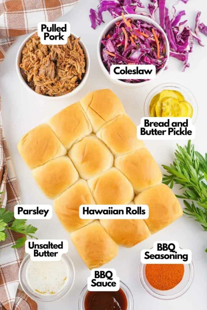 Ingredients for making pulled pork sliders, including pulled pork, coleslaw, Hawaiian rolls, pickles, parsley, unsalted butter, BBQ sauce, and seasoning, displayed on a kitchen counter.