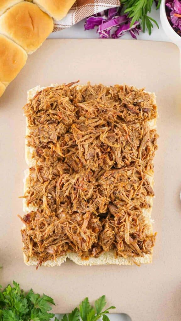 A plate of pulled pork sliders on a cutting board, surrounded by ingredients.