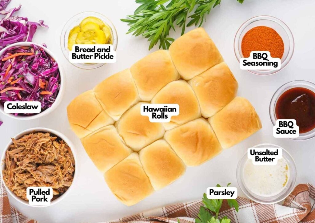 Top-down view of pulled pork sliders on Hawaiian rolls, surrounded by bowls of coleslaw, bread and butter pickles, BBQ seasoning, BBQ sauce, unsalted butter, and parsley.