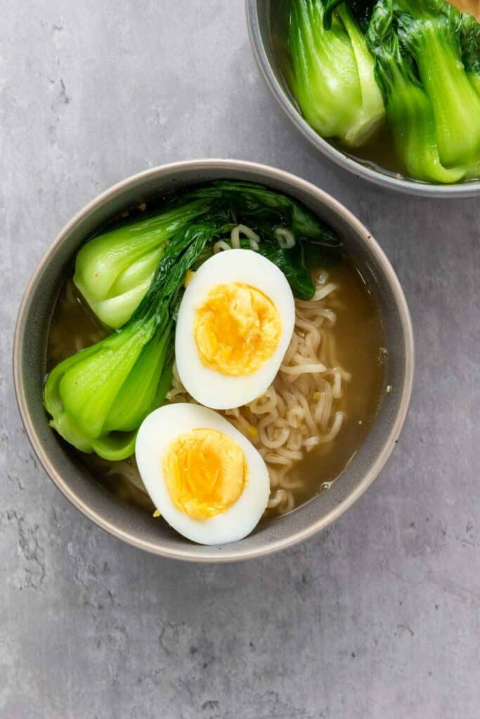 A bowl of elevated ramen noodles with halved boiled eggs and bok choy.