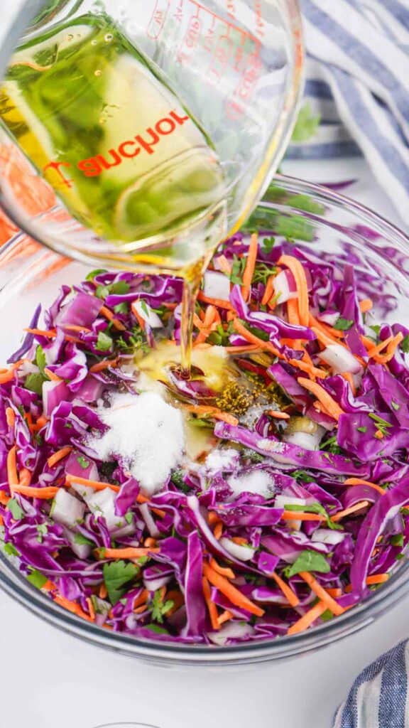 Pouring dressing on a colorful bowl of red cabbage and carrot slaw.