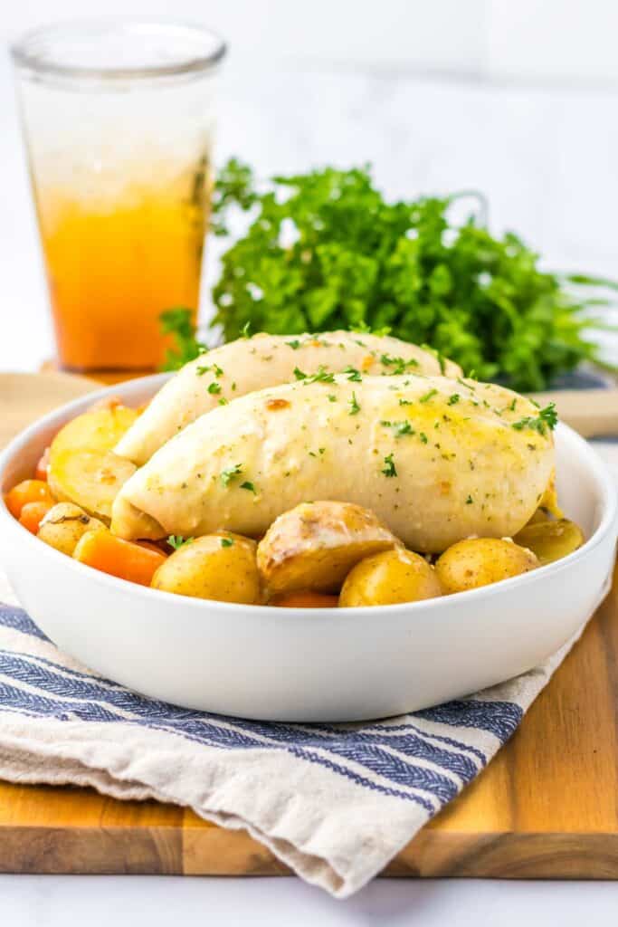 A bowl of slow cooker ranch chicken and potatoes garnished with parsley, served with a glass of iced tea.