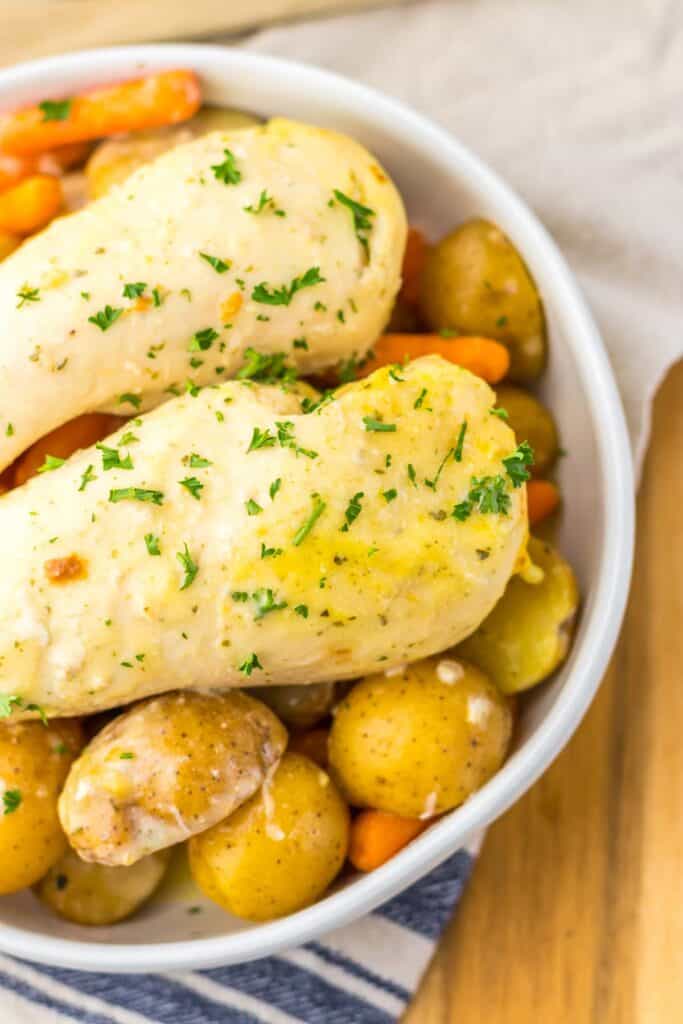 A bowl of slow cooker ranch chicken paired with roasted potatoes and carrots, garnished with chopped parsley.