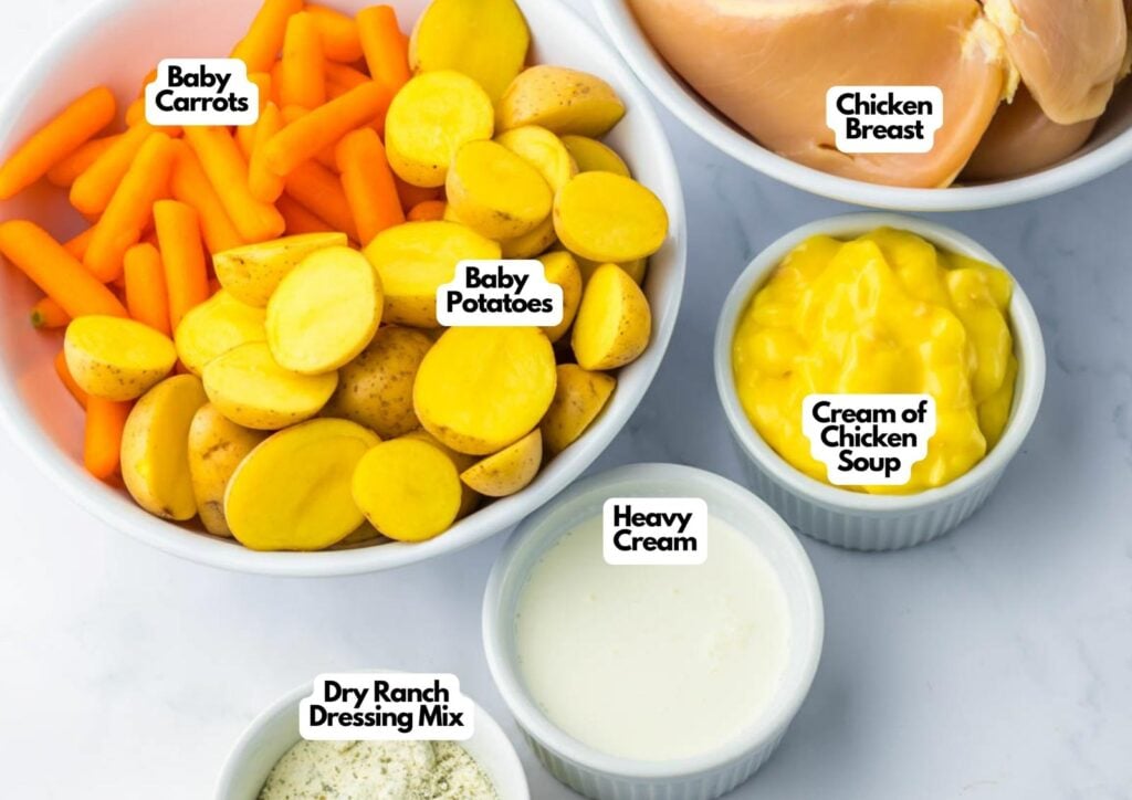 Bowls containing baby carrots, sliced baby potatoes, chicken breast, cream of chicken soup, heavy cream, and dry ranch dressing mix are arranged on a white surface—perfect for making slow cooker ranch chicken.