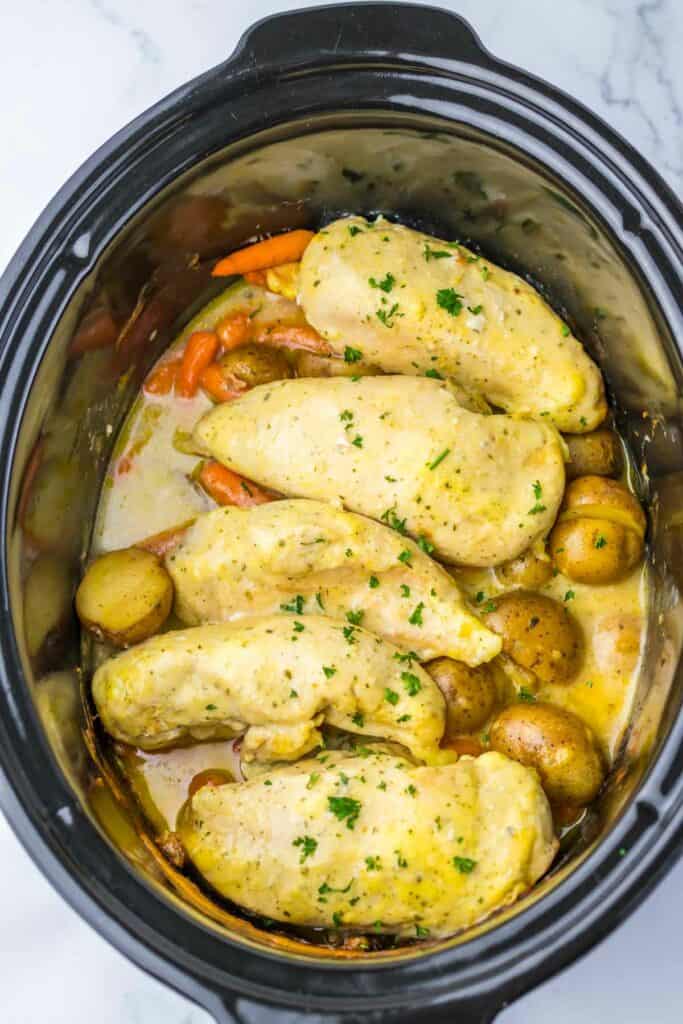 Chicken breasts with potatoes and carrots in a slow cooker, garnished with ranch and parsley.