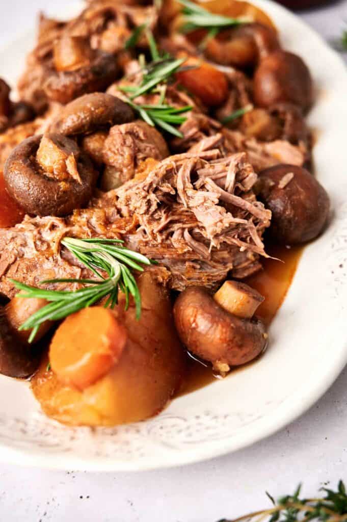 Slow cooker pot roast with carrots and mushrooms garnished with fresh rosemary on a plate.