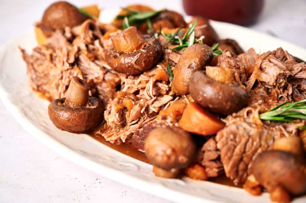 Slow cooker pot roast with carrots and mushrooms garnished with fresh rosemary on a plate.
