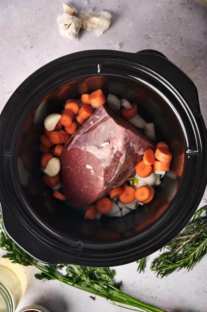 A slow cooker pot roast with carrots and onions, ready to be cooked.