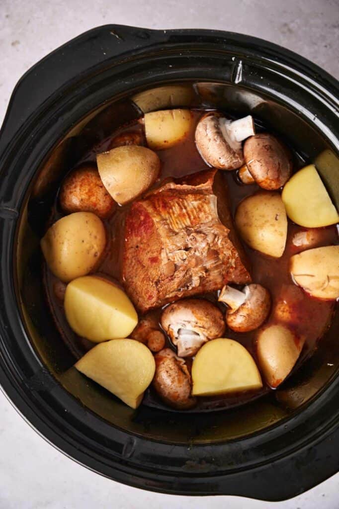 A slow cooker pot roast with beef, potatoes, and mushrooms in broth.