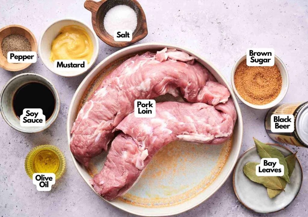 Raw pork loin on a plate surrounded by labeled ingredients: pepper, mustard, salt, brown sugar, soy sauce, olive oil, black beer, and bay leaves—perfect for making flavorful Slow Cooker Pulled Pork.