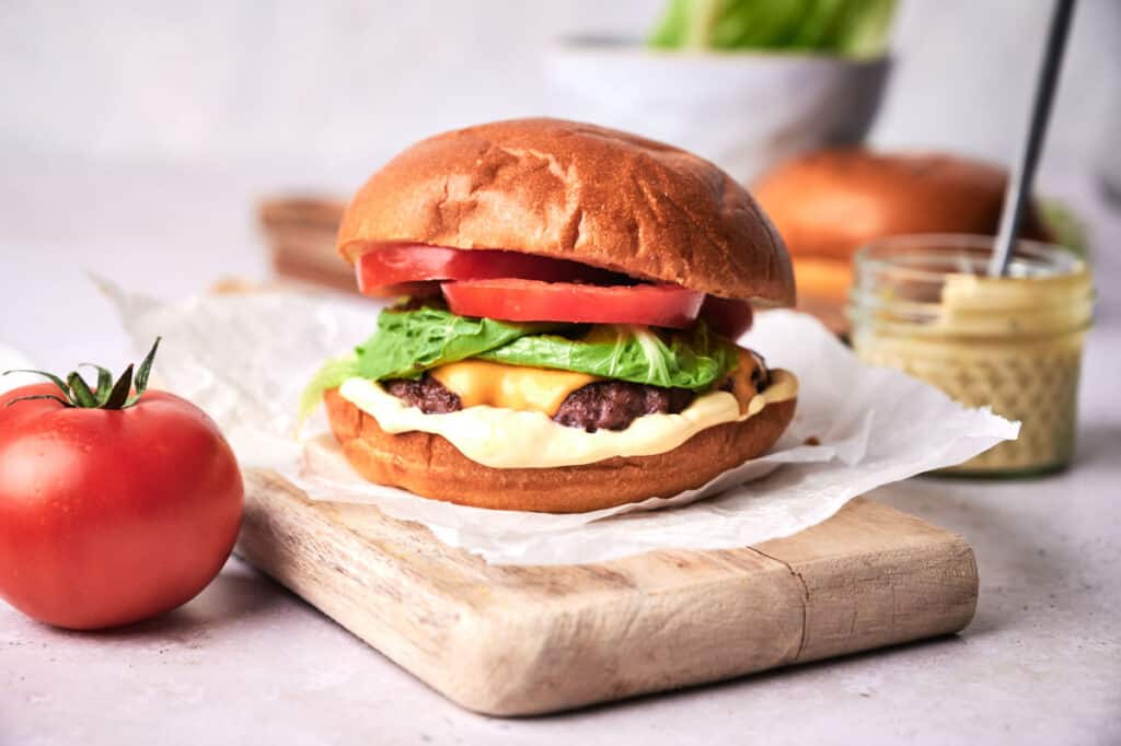 Smash burger on a board with a tomato on the side.