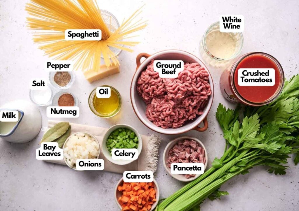 Ingredients for spaghetti bolognese are arranged on a counter, each labeled, including ground beef, spaghetti, vegetables, spices, milk, oil, wine, and crushed tomatoes for a classic Italian dish.