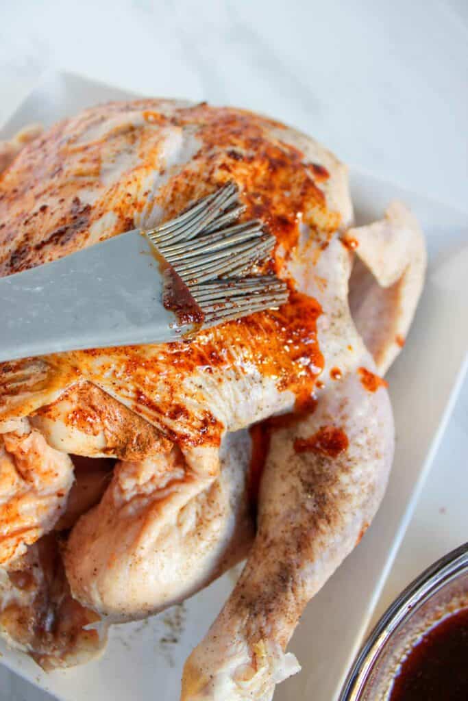 Applying marinade to a raw, spiced whole chicken with a brush.