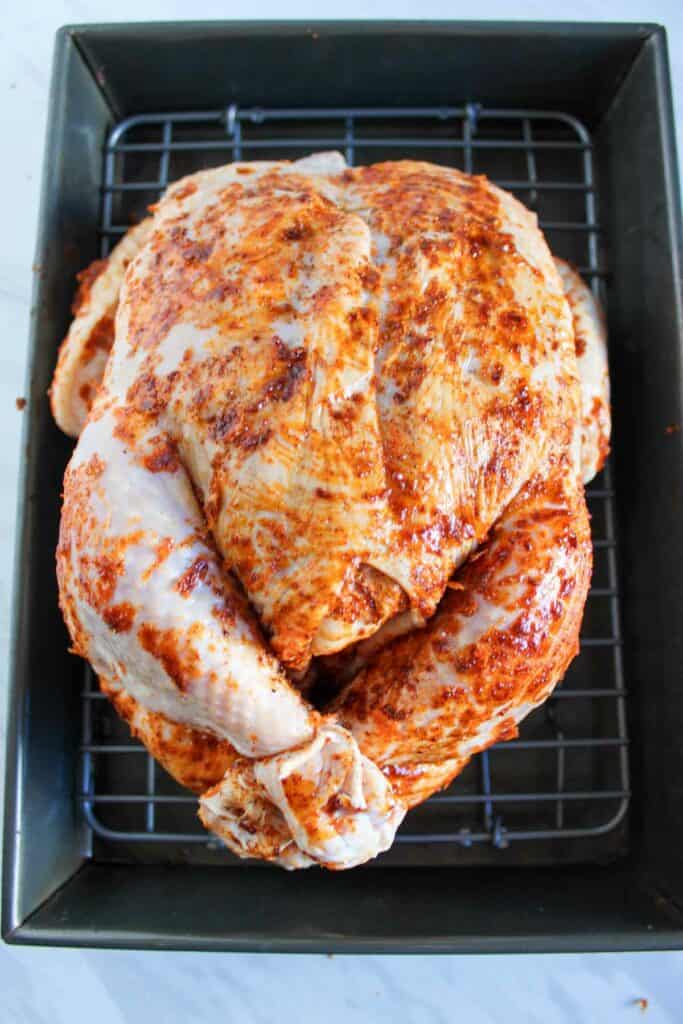 A whole raw chicken seasoned and ready to be roasted in a baking tray.