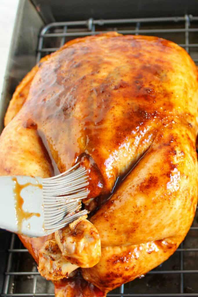 Basting a whole roasted chicken with a BBQ glaze on a cooking rack.
