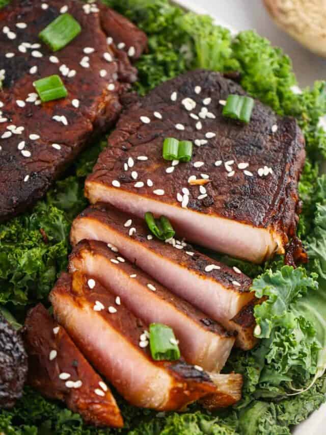 Sliced grilled pork belly garnished with sesame seeds and green onions, served on a bed of kale.